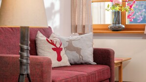 A red sofa with two decorative pillows, a lamp, and a vase with flowers on a windowsill. - Ein-Raum-Ferienwohnung (2) 28qm, Dusche/WC, Küchenzeile, Balkon (Reit im Winkl)