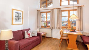 A cozy living room with a red sofa, a wooden coffee table, and a dining table with a lamp. - Ein-Raum-Ferienwohnung (2) 28qm, Dusche/WC, Küchenzeile, Balkon (Reit im Winkl)