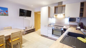A modern kitchen with a built-in oven, microwave, and a large island with a sink. There is a dining area with a wooden table and chairs.