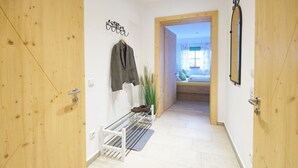 A hallway with wooden doors, a coat rack, a shoe rack, and a view into a room with a bed and window.