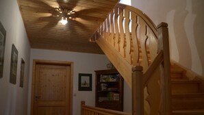Una escalera de madera con barandilla conduce a un rellano. Se ve una puerta de madera y una estantería con libros y un jarrón en el rellano.