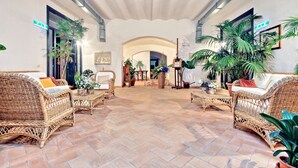 A spacious lobby with wicker furniture, potted plants, and a tiled floor. - Casale Doria Pamphilj (Fiumicino)