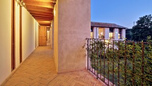 A corridor with wooden beams and a tiled floor leading to a balcony with a metal railing and greenery. - Casale Doria Pamphilj (Fiumicino)