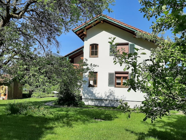 Une maison à deux étages, avec une façade blanche, des volets verts et un toit recouvert de tuiles rouges.