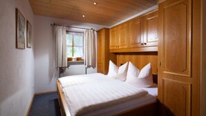 Een slaapkamer met een houten bed, een raam met gordijnen en houten kasten.