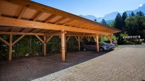 Een overdekte houten parkeerplaats met geparkeerde auto's, omringd door bomen en bergen op de achtergrond.