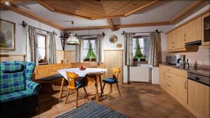Een gezellige kamer met een eettafel, stoelen, een bank en een keuken met kastjes en apparatuur.
