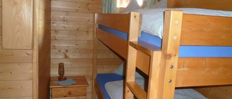 Habitació de cabana de fusta amb lliteres, un petit calaixera de fusta i una finestra amb cortines.