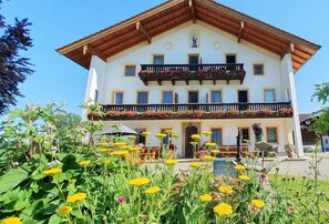A two-story building with a balcony, surrounded by a garden with various flowers. - Ferienwohnung Nr. 3 mit Südbalkon, 50qm (Seebruck)