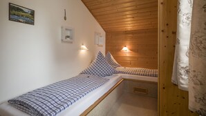 Habitació petita i acollidora amb sostre i parets de fusta, un llit amb roba de llit a quadradets, una taula petita i un aparell de ràdio penjat a la paret.