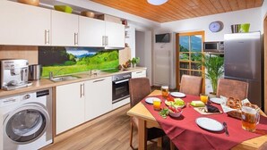 Een moderne keuken met een eethoek, voorzien van een wasmachine, een koffiezetapparaat en een televisie waarop een schilderachtige landscape te zien is.