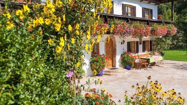 Een klassiek chalet met een balkon versierd met bloemen, een stenen terras met zitplaatsen en een weelderige tuin.