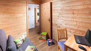 Een kamer met houten wanden en vloeren, een bank, een houten tafel met een laptop en kinderspeelgoed.