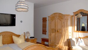 A bedroom with a wooden bed, a bedside table with a lamp, a wardrobe, and a television mounted on the wall. - 2. Fewo Zahmer Kaiser, 25 qm, 1-2 Pers., Wohn-Schlafraum, Westbalkon (Grassau)