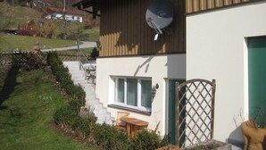 A two-story house with a satellite dish, a wooden deck, and a small garden. - Ferienwohnung für 1-2 Personen (Marktschellenberg)