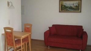 A room with a wooden dining table and chairs, a red sofa, a painting on the wall, and a light fixture. - Ferienwohnung für 1-2 Personen (Marktschellenberg)