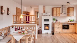 A cozy kitchen with wooden cabinets, a fireplace, and a dining area with a bench and table. - Jasmin vacation apartment with south-facing terrace and mountain view (Ruhpolding)