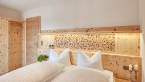 A bedroom with a wooden headboard, a bed with white bedding, a nightstand with two candles, and a small plant on the dresser. - Jasmin vacation apartment with south-facing terrace and mountain view (Ruhpolding)