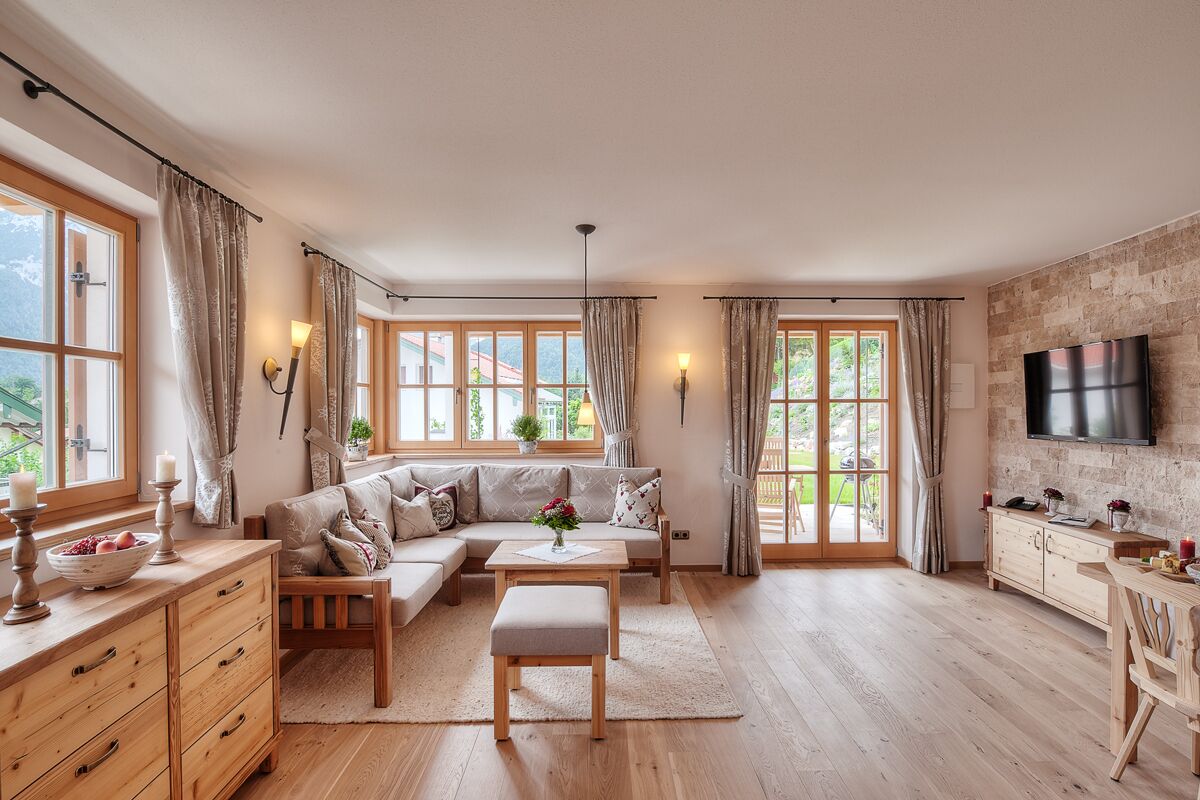A spacious living room with a sofa set, wooden furniture, and large windows.