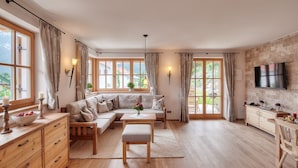 A spacious living room with a sofa set, wooden furniture, and large windows. - Jasmin vacation apartment with south-facing terrace and mountain view (Ruhpolding)