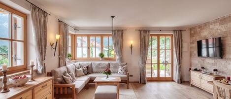 A spacious living room with a sofa set, wooden furniture, and large windows.