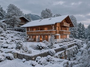 Una cabaña de madera de varios pisos con balcones, rodeada de árboles cubiertos de nieve y un paisaje montañoso.