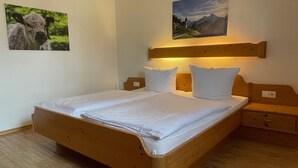 A wooden bed with white linens, a nightstand, and a wall-mounted lamp. - Apartment no. 4, 1-2 persons, 60 sqm, combined living room/bedroom, terrace (Schönau am Königssee)