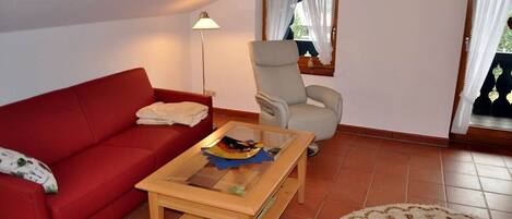 A living room with a red sofa, a beige armchair, a wooden coffee table, and a floor lamp.