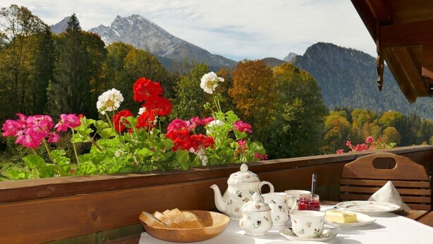 A wooden table set with tea service and bread, overlooking a mountainous landscape with colorful flowers. - Ferienwohnung 2 bis 4 Personen, 60 qm, 2 Schlafzimmer, Balkon (Schönau am Königssee)