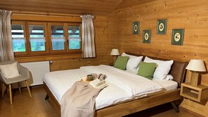 A wooden cabin bedroom with a bed, a chair, a radiator, and framed pictures on the wall. - Ferienwohnung 2 bis 4 Personen, 60 qm, 2 Schlafzimmer, Balkon (Schönau am Königssee)