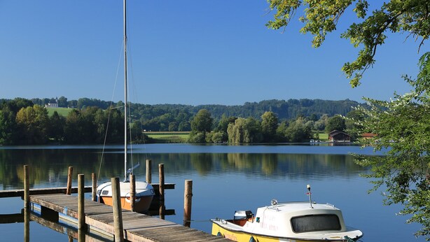 A calm lake with a wooden dock and a small yellow boat docked at the pier.
