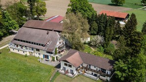 An aerial view of a large estate with multiple buildings, including a main house with a large balcony and a smaller attached structure.