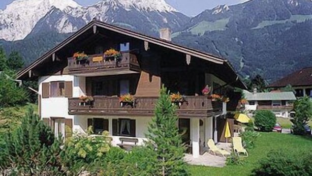 Eine Chalet mit Balkon, umgeben von üppigem Grün und Bergen im Hintergrund.