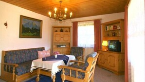 Ein gemütliches Wohnzimmer mit Holzbalkendecke, einem Sofa, einem Tisch und einem Fernseher.
