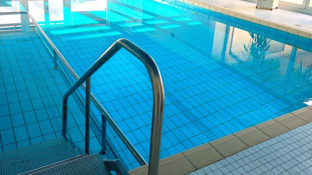 An indoor swimming pool with clear blue water, metal railings, and a tiled floor.