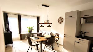 A modern kitchen with a dining area, featuring a wooden table, chairs, and a hanging light fixture.