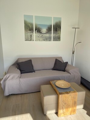 En moderne stue med en grå sofa, to sorte puder, et træsofabord og en gulvlampe.