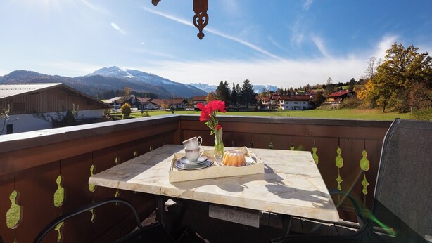 Un balcón con una mesa para dos personas, un florero con flores y vistas a la montaña.