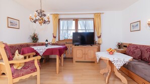 Una sala de estar acogedora con un sofá de madera, una mesa de comedor de madera con mantel rojo, un televisor y una araña.