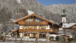 Un chalet de madera grande con balcón, rodeado de árboles cubiertos de nieve y un paisaje montañoso.