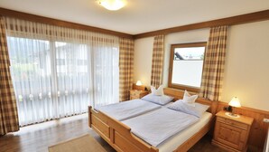 A double bed with two nightstands, a window with curtains, and a wooden floor. - Ferienwohnung Fellhorn (Reit im Winkl)