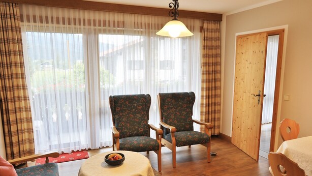 Ein Zimmer mit zwei floralen Ohrensesseln, einem kleinen Tisch mit einer Schale und einer Holztür.