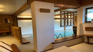 Un cuarto de spa con una camilla de masaje, bancos de madera, un ventanal con vistas y una zona de piscina.