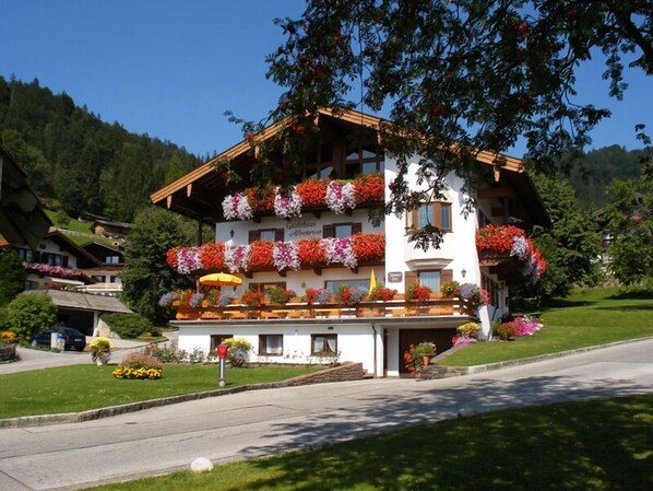 A two-story building with balconies adorned with flowers, a sign indicating it is a guesthouse, and a clear view of the surrounding greenery.