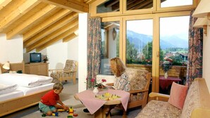 A cozy room with a bed, a sofa, a table with a vase, and a window with a view of mountains. - (8) Zwei-Raum-Ferienwohnung 41qm, Dusche/WC, Extra-Schlafraum, Küche, 2 Balkone (Reit im Winkl)