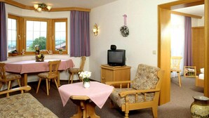 A cozy living room with a dining area, wooden furniture, a television, and a vase with flowers. - (8) Zwei-Raum-Ferienwohnung 41qm, Dusche/WC, Extra-Schlafraum, Küche, 2 Balkone (Reit im Winkl)