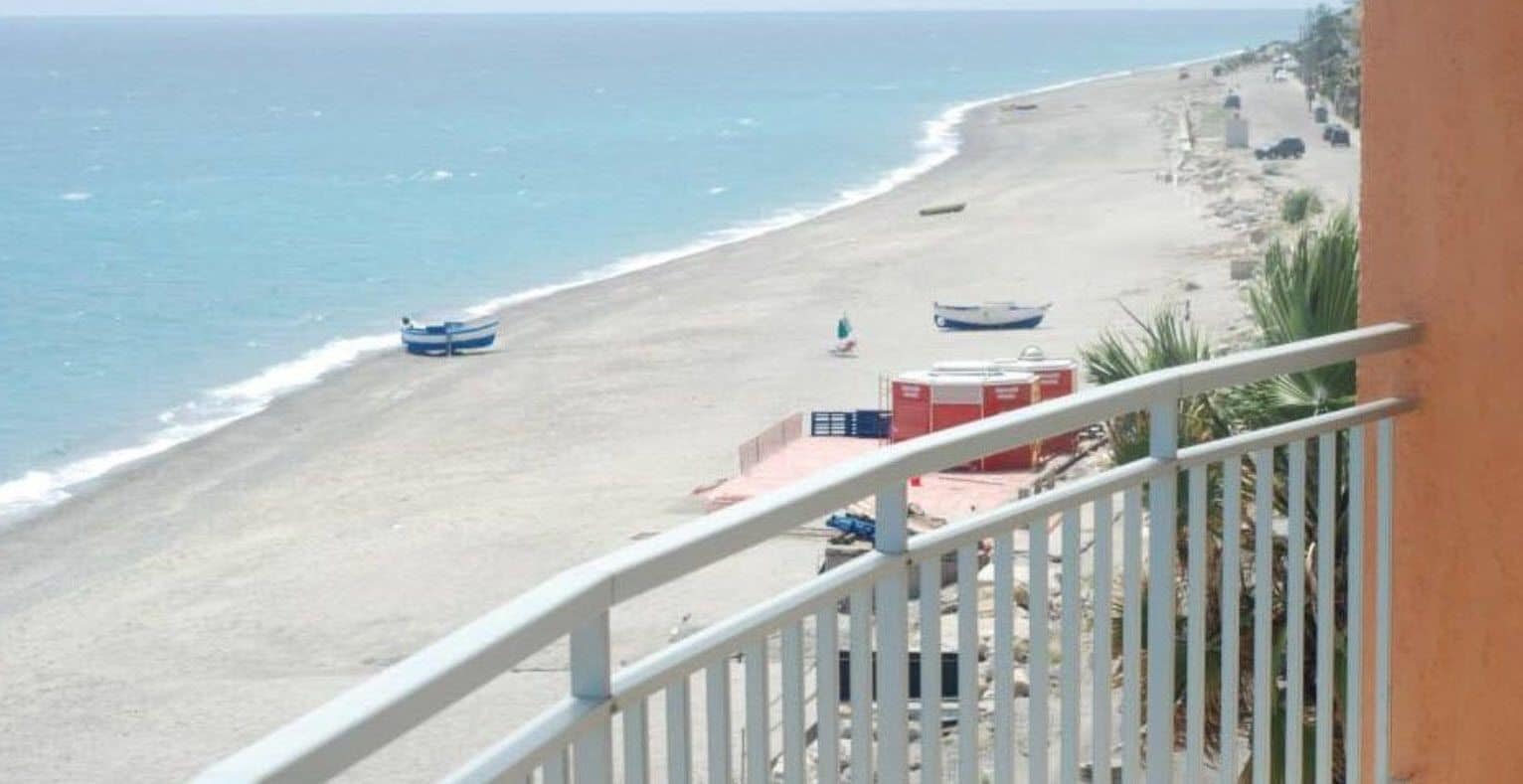 A beach with boats, a red lifeguard tower, and a white railing.
