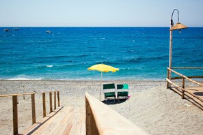 A wooden boardwalk leading to beach chairs under a yellow umbrella, overlooking the sea.