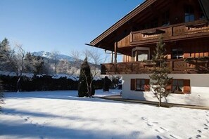 A wooden chalet with a balcony, surrounded by snow-covered ground and trees.