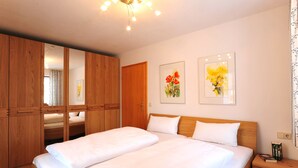 Une chambre avec un grand lit, une armoire en bois et deux tableaux floraux encadrés accrochés au mur.